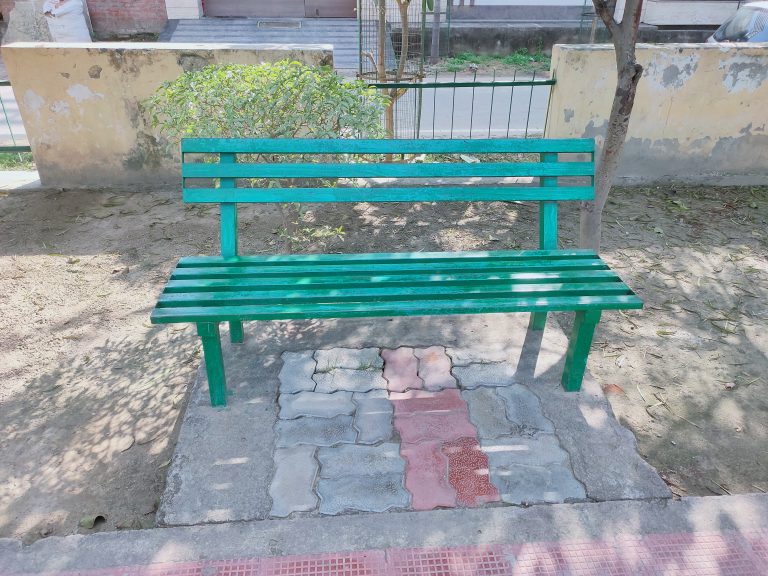 A green wooden bench in the park in the shade of a tree.