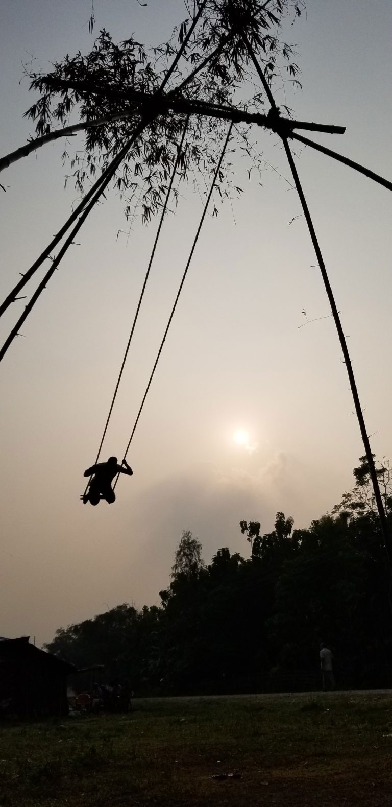 The silhouette of a person swinging on a traditional bamboo swing, also called a bamboo ping.