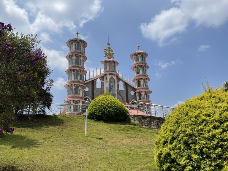 Beautiful church in Kerala situated on top of a hill with lawns and flower tress in the foreground.