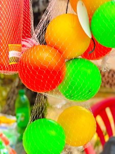 Multi coloured plastic balls hanging inside a white net on some street shop. 