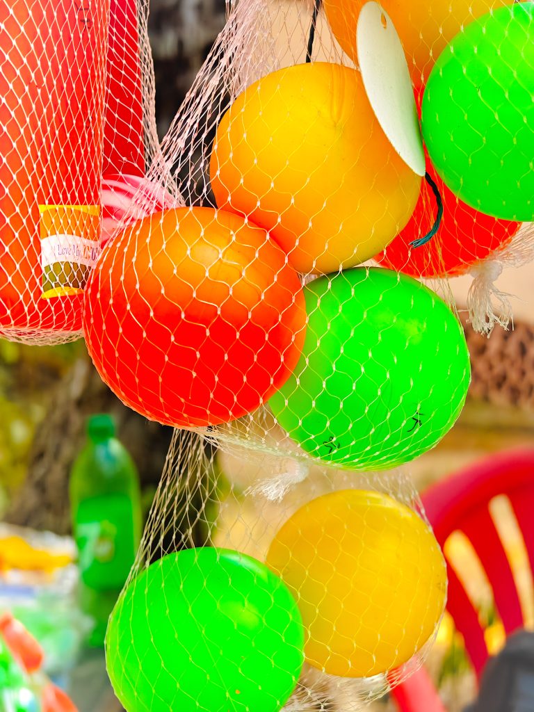 Multi coloured plastic balls hanging inside a white net on some street shop.