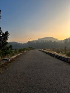 An asphalt road stretches ahead, framed by the silhouette of hills against the rising sun.
