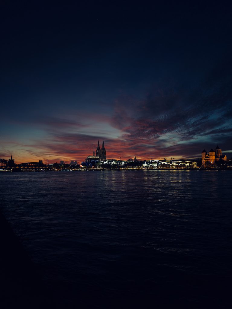 Cologne cathedral and a few buildings having illuminated windows with a dark but colorful sky during the end of sunset.