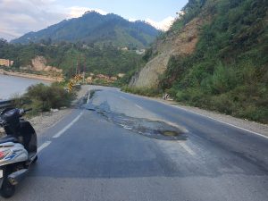 Road with a pothole and mountains with lush greenery in the background. 