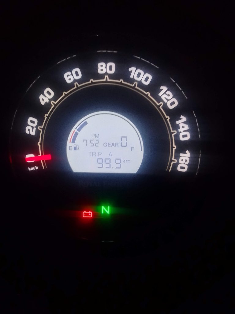 A motorcycle’s digital speedometer display shows a speed of 0 km/h, with a total trip distance of 99.9 km.