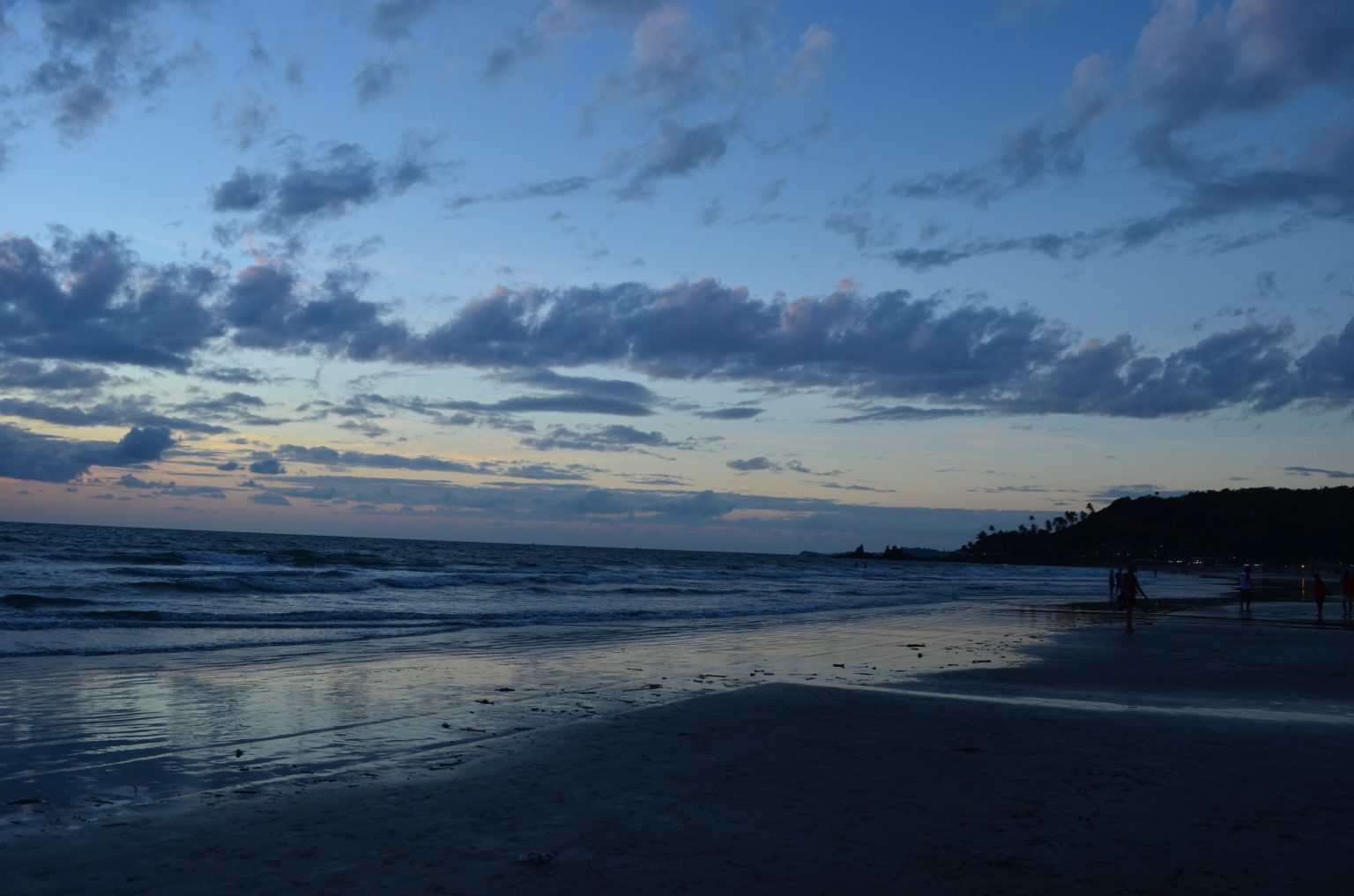 A beach at dusk with the entire sky tinged in dark blue, adorned with clouds
