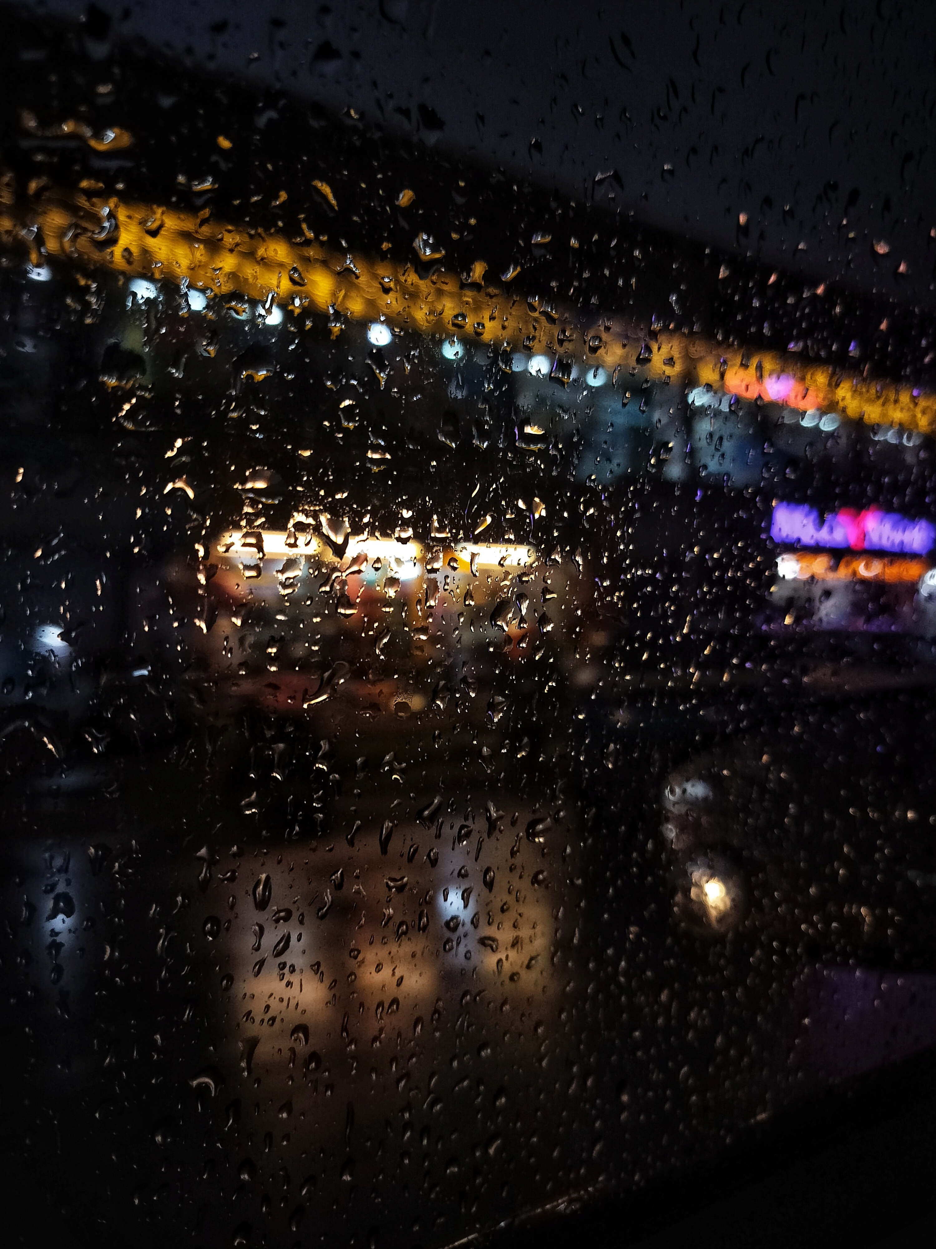 Looking through a window where raindrops capture the light beyond at night