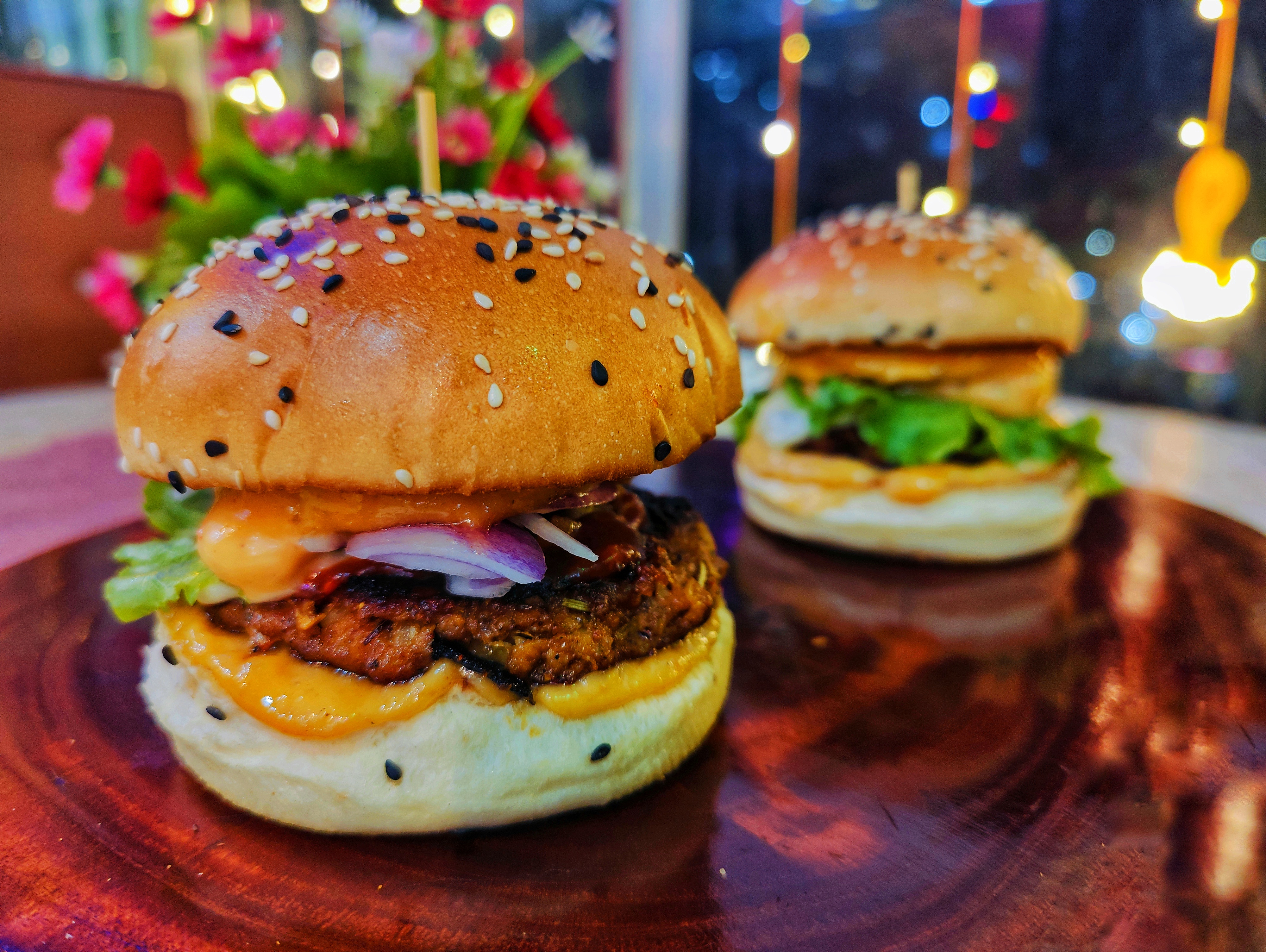 Chicken burger, garnished with cheese, red onion and lettuce. Buns sprinkled with black and white sesame seeds, presented ready to eat. 