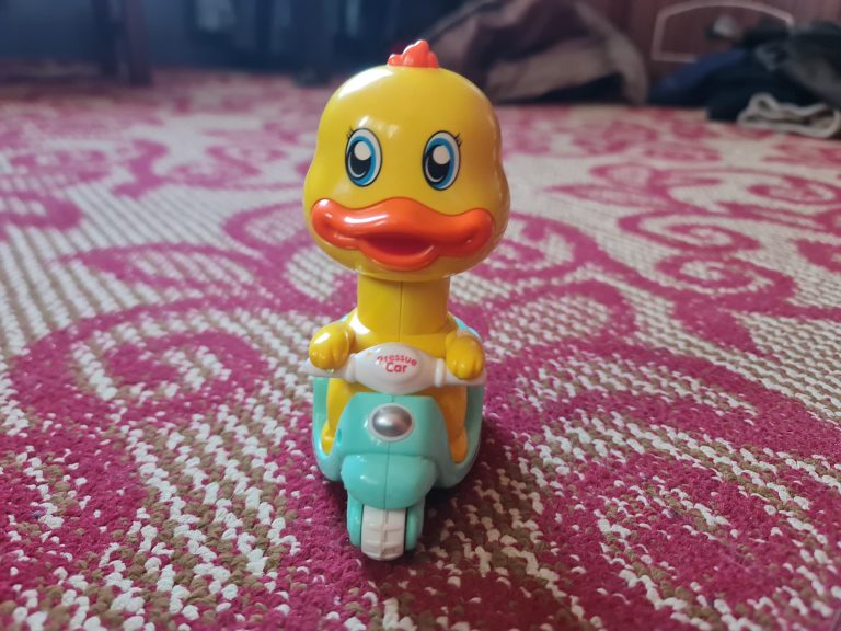 A yellow toy duck is riding a fountain blue toy motorcycle.