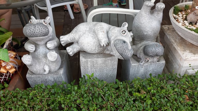 A couple of cement hippos sitting on top of cement blocks.