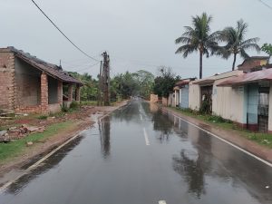 View larger photo: Rain falls on a street with buildings on either side, electric wires overhead, and palm trees.