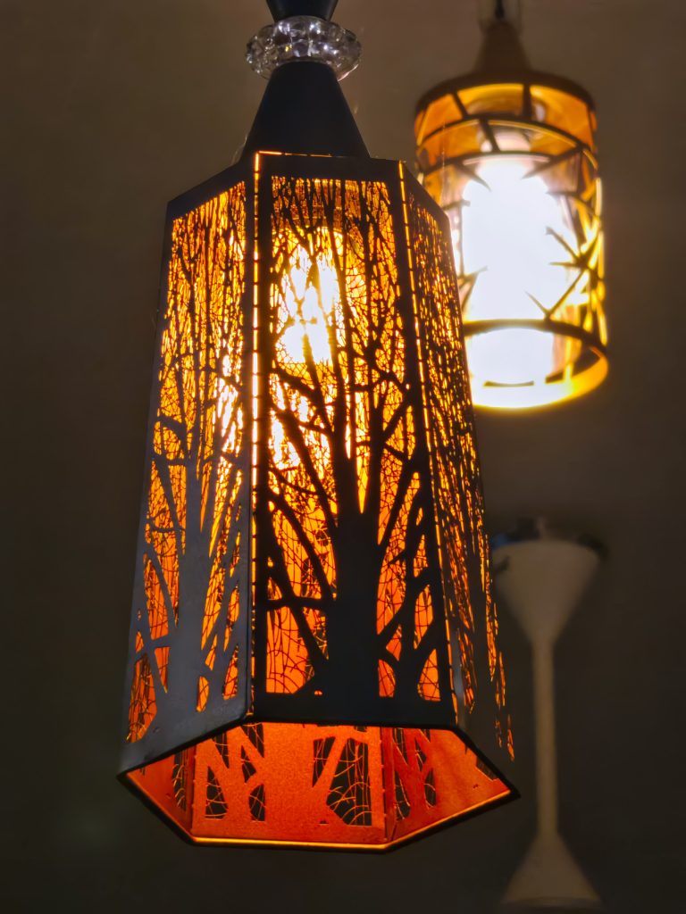 Home decor light with tree branch pattern on the sides hanging from a ceiling.