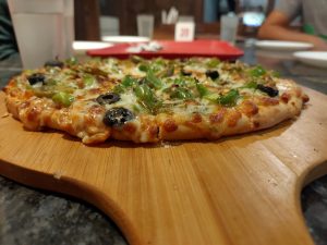 A pizza with peppers, olives, and cheese being served on a wooden board 