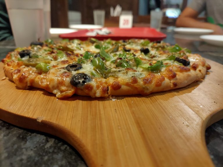 A pizza with peppers, olives, and cheese being served on a wooden board