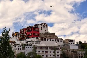 A helicopter flying over the white and red buildings of the Thiksey Monastery in Leh 