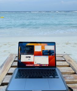 A laptop placed on a wooden table on a sandy beach. 