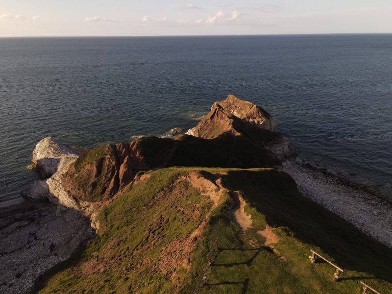 This captivating photo captures the serene beauty of the seaside near Flamborough, UK. The vast expanse of the shore is adorned with rugged rocks, standing resilient against the rhythmic dance of the waves. The soft, billowing clouds above create a dynamic play of light and shadow on the landscape.