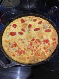 A vegetable frittata with cut tomatoes on top in a cast-iron pan.
