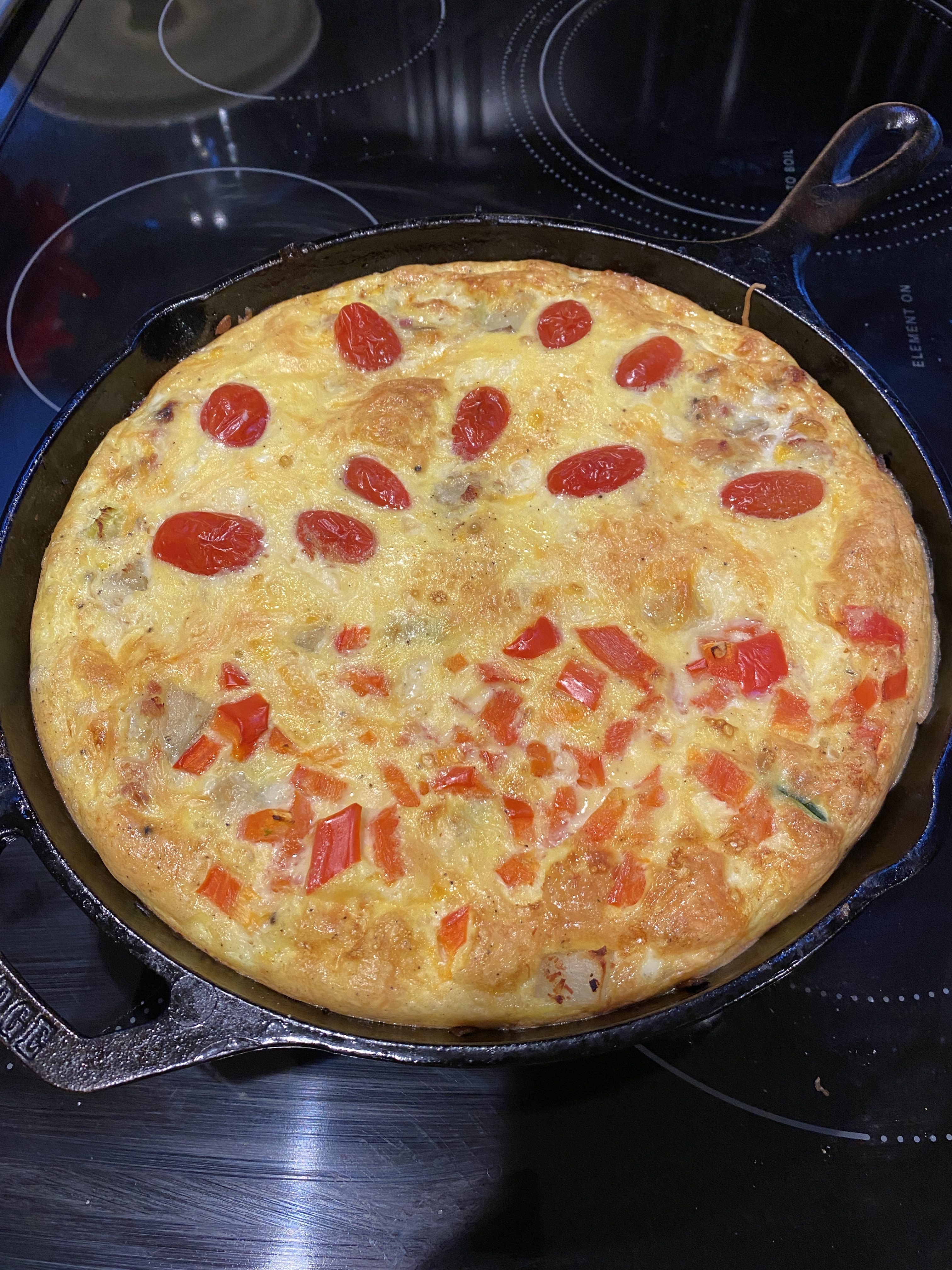 A vegetable frittata with cut tomatoes on top in a cast-iron pan.