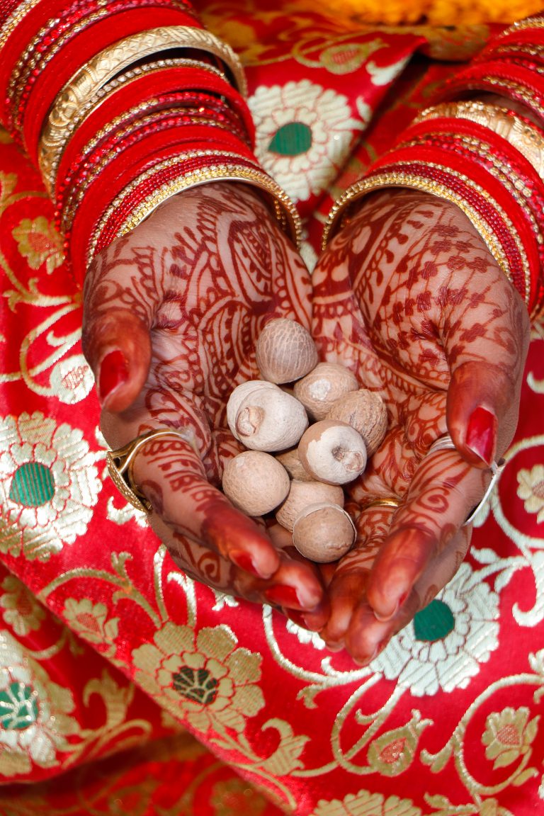 Gracefully adorned with beautiful mehendi art, hands intertwined around a betel nut, signifying the sacredness of a marriage ceremony.