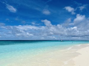 A view of a beautiful beach and a clear blue sky with some white clouds and people are enjoying swimming.