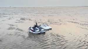 A serene low tide scene at Alibaug, Mumbai, with visitors' shoes on the sand and a distant boat, embodying a peaceful beach escape. 