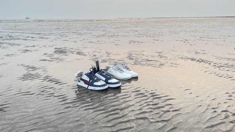 A serene low tide scene at Alibaug, Mumbai, with visitors’ shoes on the sand and a distant boat, embodying a peaceful beach escape.