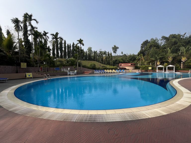 A swimming pool is situated in the front, surrounded by trees in the background.