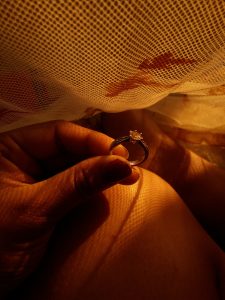 View larger photo: A hand holding a diamond ring illuminated by yellow light coming through a mesh fabric.