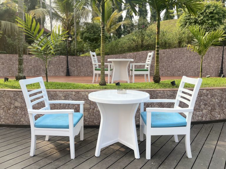 Chairs and tables in a white color, set against a backdrop of trees and plants.