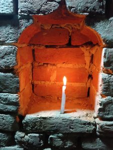 A candle illuminates a historical wardrobe almirah, crafted by cutting the wall bricks in a pattern, in an Indian village.