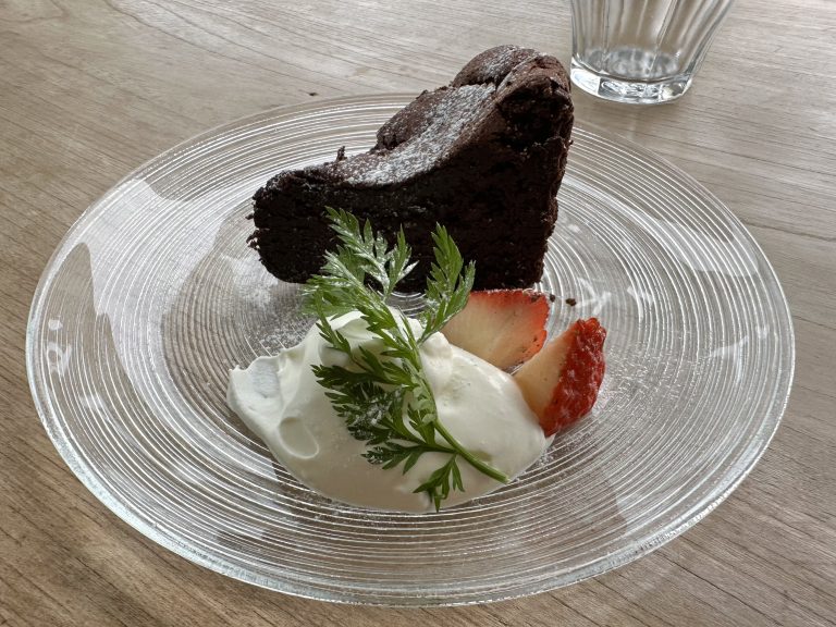 A piece of chocolate fudge cake with whipped cream and slices of strawberry on a glass plate at a cafe.  Coffee shop, sweets, dessert, brownie, cocoa cake, gateau, sponge.