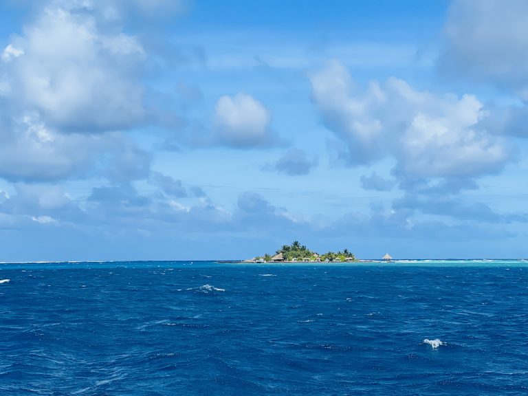 Beach island surrounded by very blue water on a sunny day with white fluffy clouds in the sky.