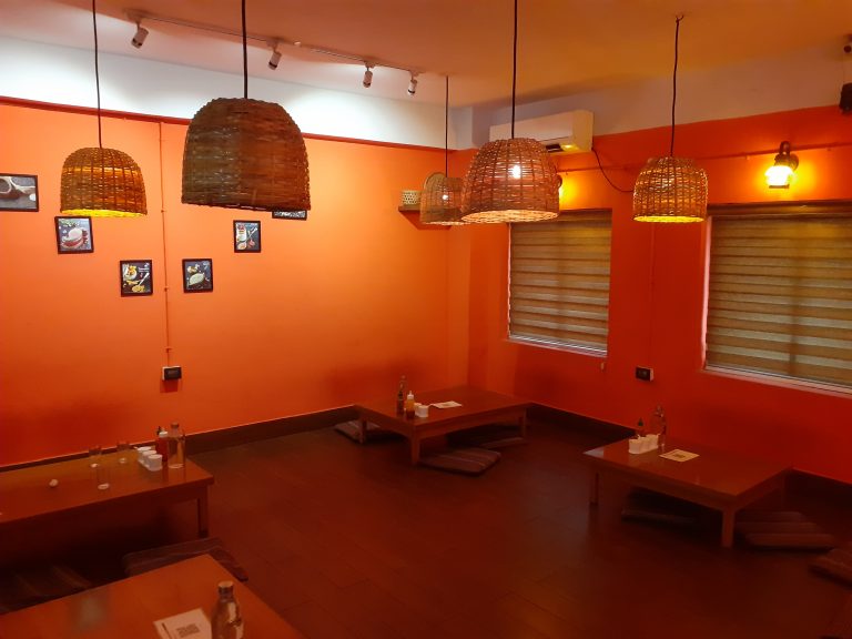 The orange interior! A room with orange wall and lights hanging from the roof. Also, there is table with bottles on the top and cushions to sit around it.