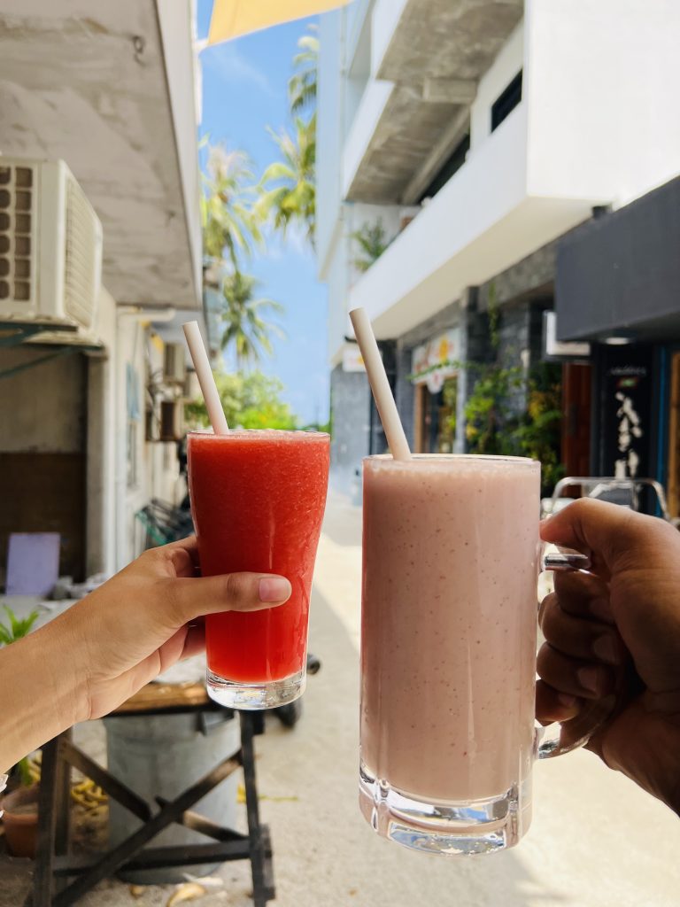 Smoothie and juice held in glasses outdoors in sunlight