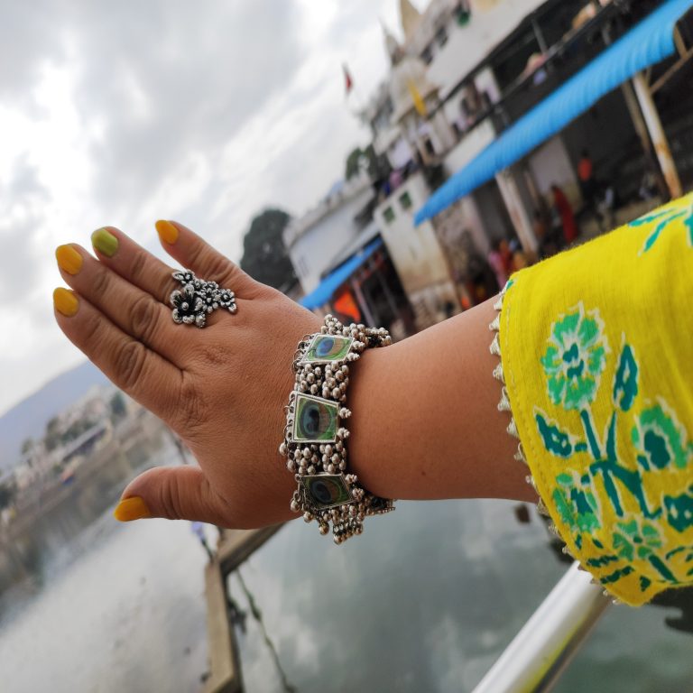 A woman’s hand adorned with a yellow manicure and a bracelet, showcasing the elegance of peacock jewelry.