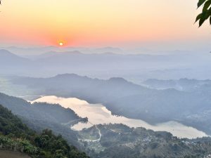 Sunset setting over a mountain ranges with fog and a lake and township in the valley. Pokhra Lake. 