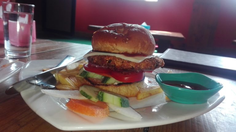 A burger is on a plate with spoons, sauce, and a glass of water.