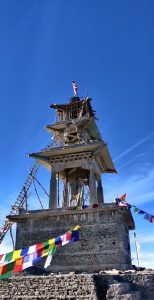 The temple, currently being built, is surrounded by prayer flags with a backdrop of a blue sky.  