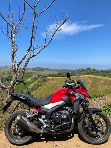 A striking red motorcycle stands against the backdrop of majestic hills.