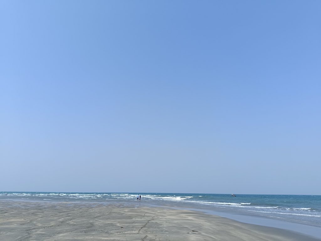 Beach with clear blue sky, gentle waves, and distant figures under the vastness of an open horizon.