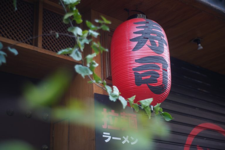 Big red Chinese paper lantern hanging from the roof of a building.