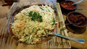 Chicken fried rice served on a wooden plate in a restaurant in Galle, Sri Lanka. The side dishes are spicy prepared using dates and red chillies.