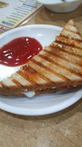 The grilled sandwich with red tomato sauce is served on a white plate.