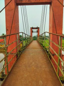 An old red coloured bridge with rusty handrail.