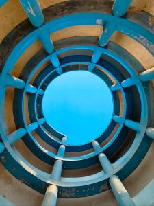 The inside view of watch tower from its bottom that creates a clear view of blue sky and the stairs up to top of tower
