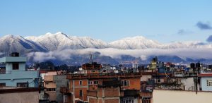 A cityscape with low clouds and snow covered mountains in the background