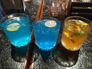 Three colorful drinks on a table: two blue cocktails and a yellow lemonade.