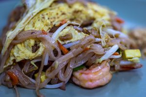 A close up of pad Thai featuring a single shrimp on a blue plate.  
