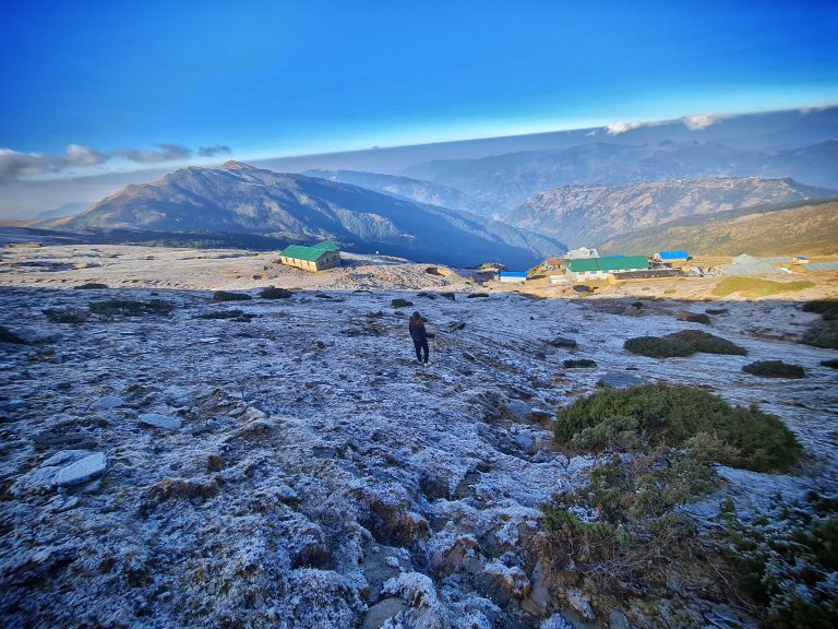 A person walks down a snow-covered downhill slope, a beautiful mountain, and a clear blue sky in the background.